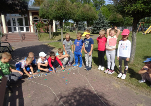 dzieci bawią się w wyścigi kapselkami, mają narysowany start z miejscami startowymi kredą na chodniku